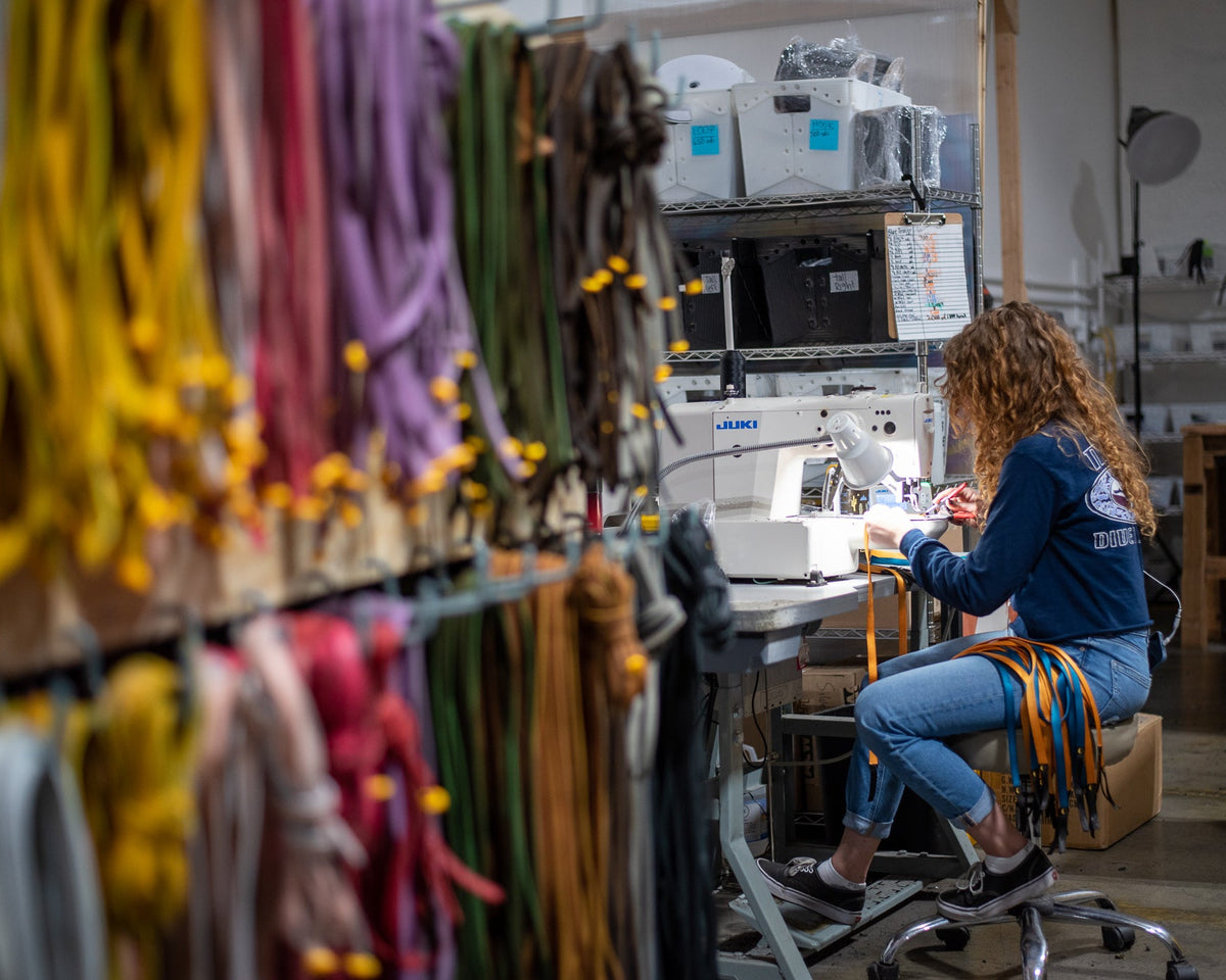 The LUNA workshop in Wenatchee. A wall of coloured laces in the foreground and a maker at a Juki sewing machine behind them.