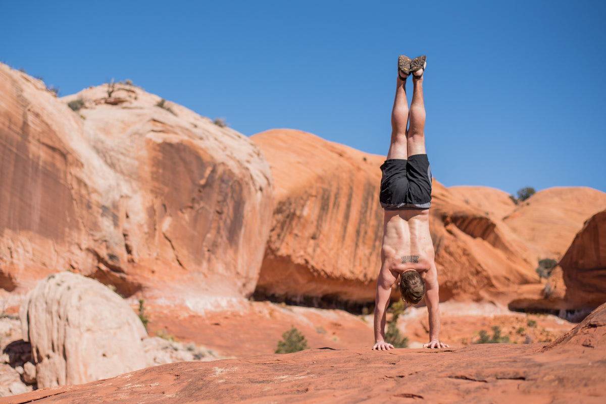 A person holding a handstand on smooth red sandstone in the Escalante desert, wearing LUNA sandals.