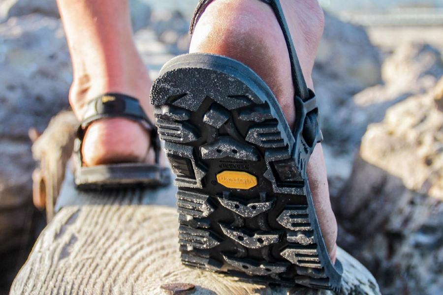 A foot in a Middle Bear sandal stepping along a fallen log, the lugged Vibram outsole facing the camera.