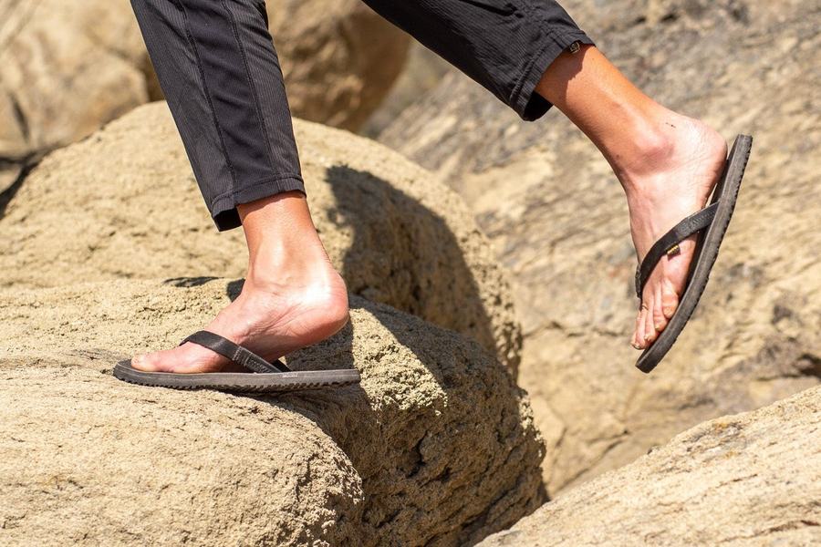 Legs in LUNA Chanclas stepping across sunlit boulders.