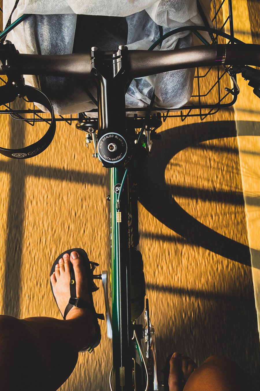 Looking down at a foot in a LUNA on a bike pedal, low sun throwing long shadows across the road.